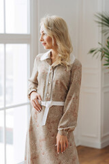 adult young woman is resting in a beautiful feminine blue dress in a bright room by the window...