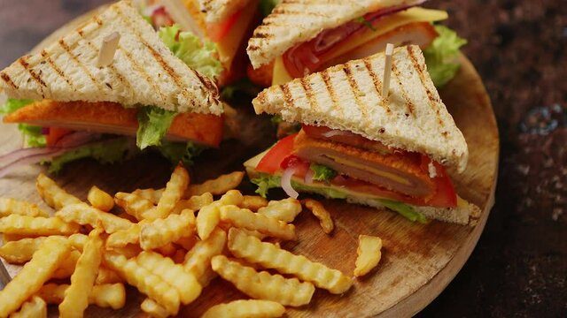 Club sandwiches served on a wooden board. With hot French fries