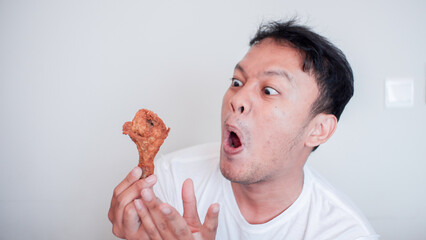 Young Asian man is eating fried chicken wear white shirt feeling angry and mad