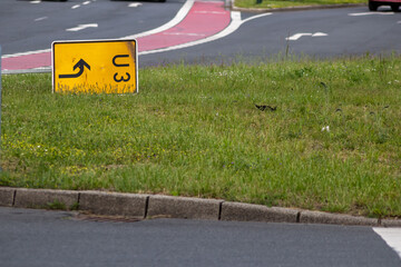 Yellow traffic sign for redirection on urban streets forces navigation system to calculate a new route for correct routing to reach your destination on German roads lying on grass after heavy storm