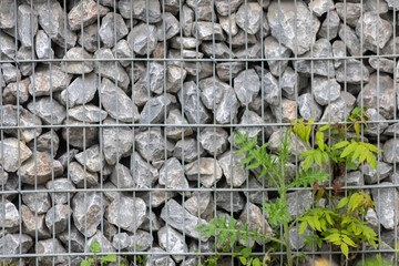 Protective gabions with grey broken stones behind grid as solid fence and solid wall and decorative element in gardens with rough surface textured as rock background and natural modern architecture