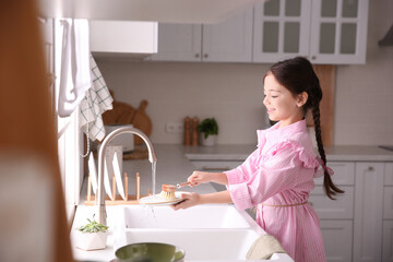 Little girl washing dishes in kitchen at home