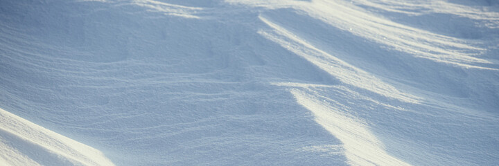 Beautiful winter background with snowy ground. Natural snow texture. Wind sculpted patterns on snow surface. Wide panoramic texture for background and design.