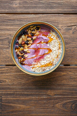 smoothie bowl with mango and berries hold by hands over wooden table