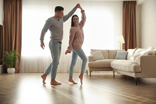 Happy couple dancing barefoot in living room. Floor heating system