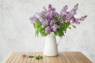 Still life with a blooming branch of lilac flowers in vase on an artistic background