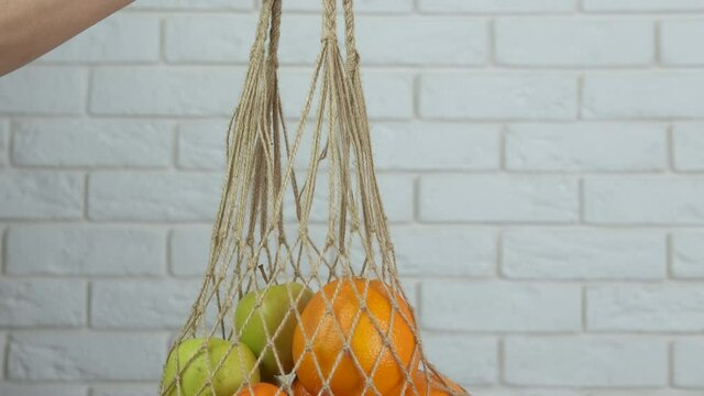 Summer fruits in a string bag. A girl hold a cotton string bag with organic fruits in it in the room.
