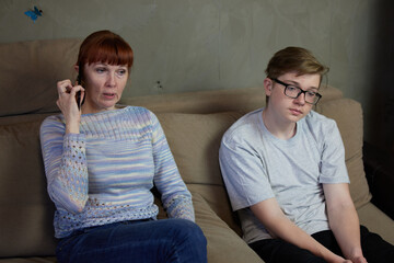 High resolution photo mother talking on phone next to indifferent son at home