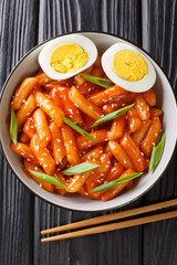Korean tteokbokki spicy rice cake with eggs close-up in a bowl on the table. Vertical top view from...
