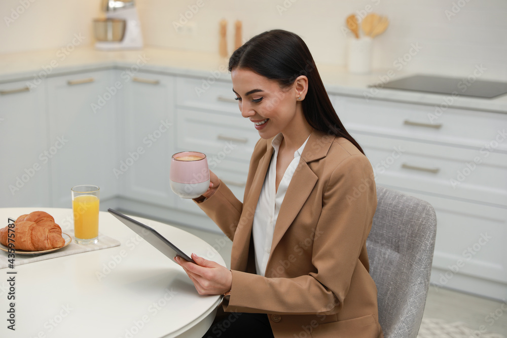 Poster Young woman with tablet having breakfast in kitchen. Morning routine