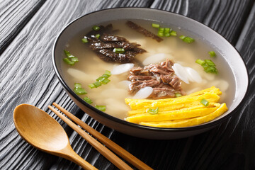 Tteokguk or sliced rice cake soup is a traditional Korean dish eaten during the celebration of the Korean New Year closeup in the bowl on the table. Horizontal