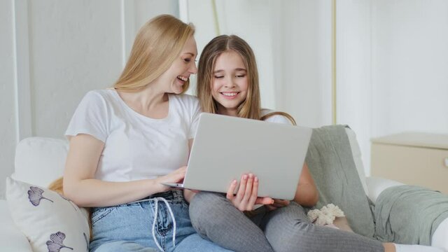 Adult mother and teenager girl daughter child sitting together on couch using modern laptop watching video funny pictures online surfing internet loudly laughing sincerely having fun browsing in net