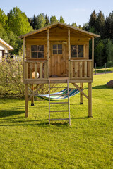 Little children's tree house with a hammock in the garden on a sunny summer day, warm and cosy environment with grass lawn, playground