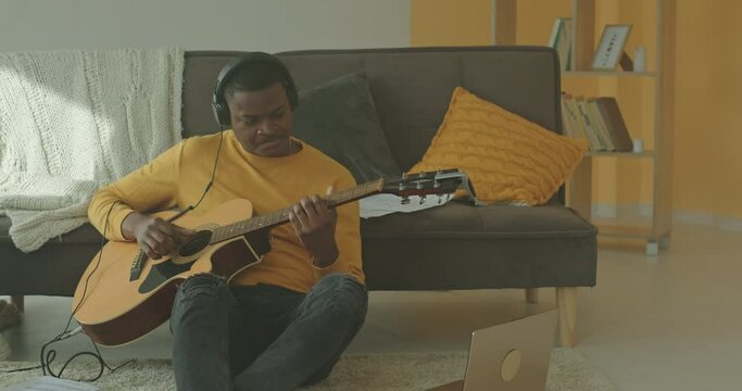 Man in headphones playing guitar at sofa