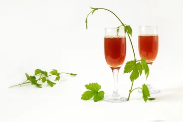 Fotobehang Two glasses of wine with leaves and branches of young hops on a light background, side view, space for text © MARYIA