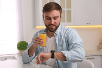 Young man with smart watch and glass of juice in kitchen