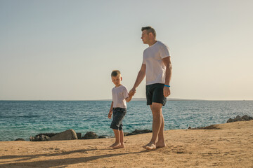 Father and  son  spending time together sea vacation. Young man, little boy walking beach Fathers day. Family with one child. Happy childhood with daddy.