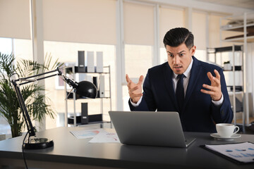 Emotional businessman with laptop at table in office