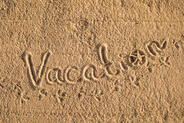 Word Vacation written in the sand on the beach.  Summer travel concept. Birds footprints on yellow sand.
