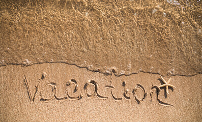 Word Vacation written in the sand on the beach.  Summer travel concept