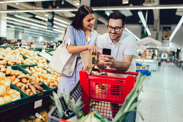 Happy couple buying vegetables at grocery store or supermarket - shopping, food, sale, consumerism - Powered by Adobe