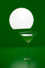 Closeup glass of classic cocktail at minimalistic green color background with spot light.