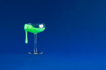 Bold vibrant neon green cocktail drink on dark blue background. Surreal minimal party concept. Celebration idea with champagne glass.