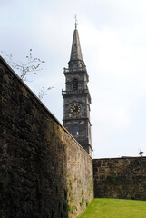 Fototapeta na wymiar Old Church Spire & Clock seen over Ancient High Stone Garden Wall 