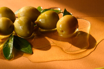 ripe olives and flowing oil, foliage and fruits on an orange background, studio shot.