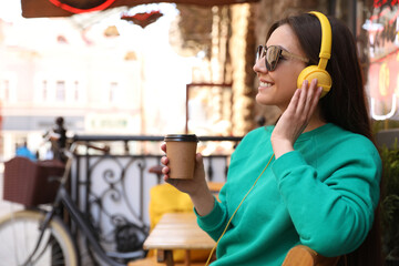 Happy young woman with coffee and headphones listening to music outdoors