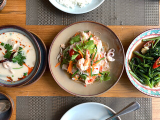 colorful spicy Thai foods traditional popular authentic Thai food served on conservative style plates on wooden table , bowl of Jasmine rice, and glass noodle spicy salad with shrimp , Top view foods