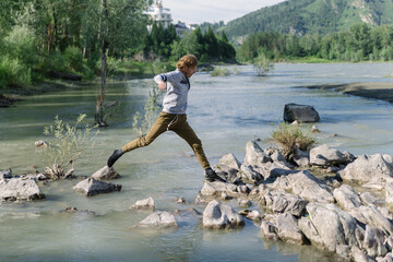 A young man walks along a mountain river, jumping from stone to stone. Hiking and traveling concept. Altai Republic