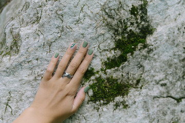 Hand with nature-inspired manicure design touching stone surface in the forest. Green shades nails. Ecology concept