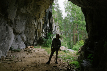 Inside view of the exit from the cave: silhouette of a young man travels in a forest. Nature of Mountain Altai