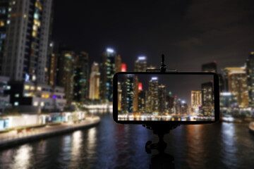 Fototapeta na wymiar DUBAI, UNITED ARAB EMIRATES - NOVEMBER 03, 2018: Night cityscape of marina district, blurred view. Taking photo with smartphone mounted on tripod