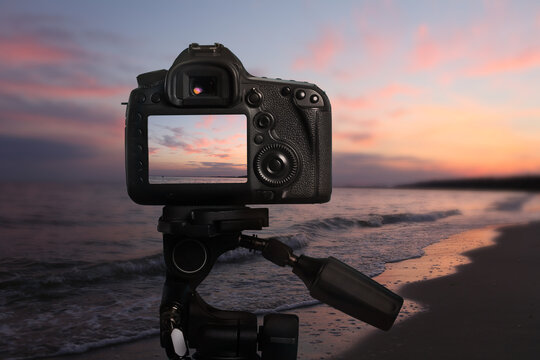 Taking photo of beautiful sandy beach at sunset with camera mounted on tripod - Powered by Adobe