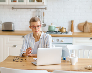 Telemedicine, video call to doctor, communication with medicine online. Modern focused middle aged woman having online call on laptop showing tablets in a blister. Healthcare and medicine concept
