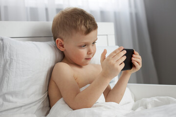 A little boy smiles sweetly while holding a black phone. Use of gadgets by preschool children