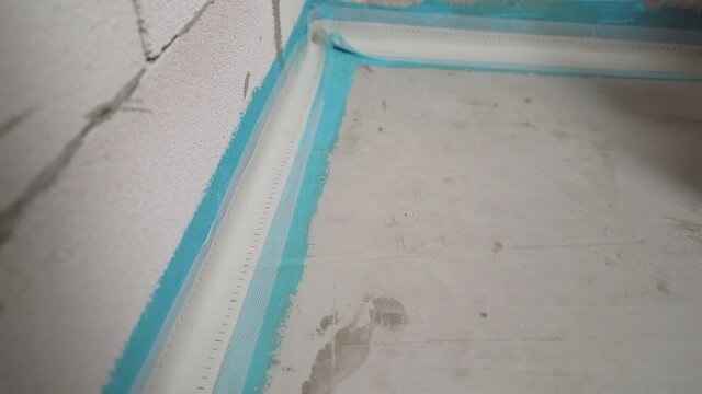 Damper tape for self-leveling floor. Worker glues damper tape before laying the floor. Reinforcing tape for drywall. Damper tape for screed. Glue the damper tape.