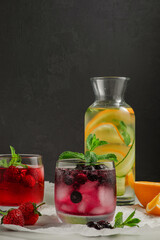 a mix of cold homemade lemonades, in glass glasses and a bottle, mint leaves, citrus slices and berries on a dark background