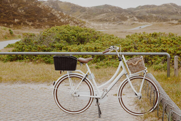 Fototapeta na wymiar White vintage ladies bicycle in the dunes by the North Sea. Vacation at the sea by bike. Bicycle parking lot in nature 