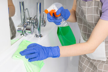 Woman doing chores in bathroom, cleaning bathtub with spray and cloth