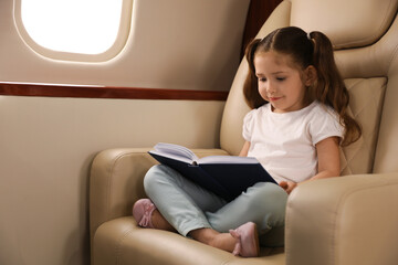 Cute little girl reading book in airplane during flight