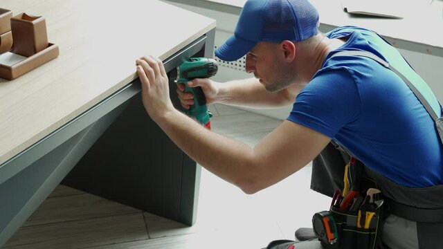 Male handyman using an electric screwdriver tool in his hand and repairing a wooden table