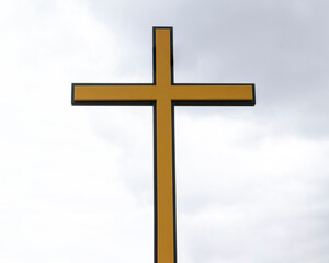 Christian Catholic cross. Color - yellow with black edging. Background - the sky with clouds. Catholic religious symbol concept.