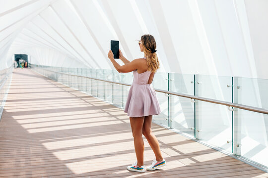 A young woman in a summer dress walks and takes a photo on a tablet
