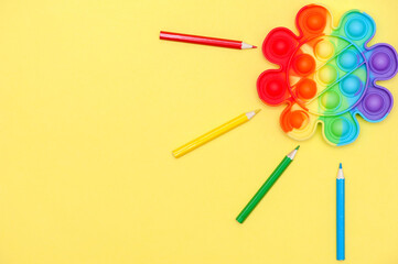 Rainbow color toy anti-stress for fingers Pop It in the shape of a flower on a yellow background. Childhood concept 