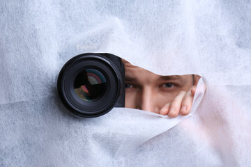 Hidden man with camera spying through hole in white fabric, closeup