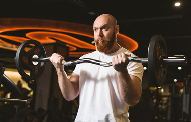Obraz na płótnie Canvas Charismatic red-bearded male bodybuilder performs barbell biceps exercise in a sports club.