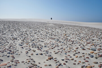 Turyści spacerują nad morzem, zdjęcie z oddali. Na pierwszym planie morski piasek w tle...